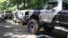 1989 Ford Bronco - Multiple off-road vehicles navigate a muddy, wooded trail, kicking up dirt and water.