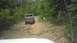 1989 Ford Bronco - A brown pickup truck navigates a challenging off-road path through a wooded area.
