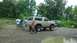 1989 Ford Bronco - A lifted tan 1987 Ford Bronco is parked on a muddy road with other vehicles and people nearby.