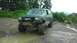 1989 Ford Bronco - This modified SUV is parked on a wet, muddy path with trees and hills in the background.