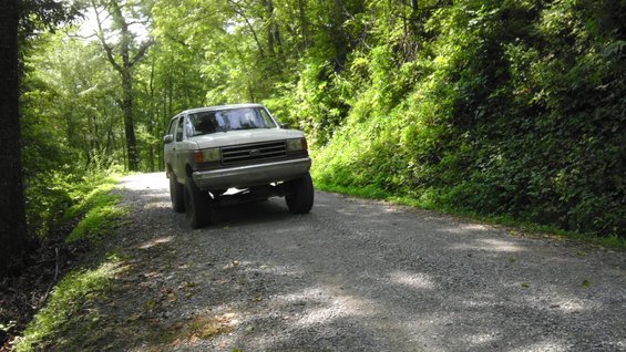 White Ford Bronco on a gravel road, front 3/4 view, lifted suspension, dirt road