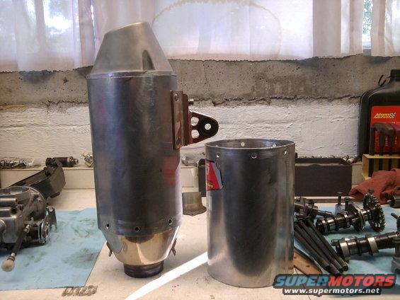 Motorcycle exhaust muffler and cylinder next to camshafts and engine parts on a workbench