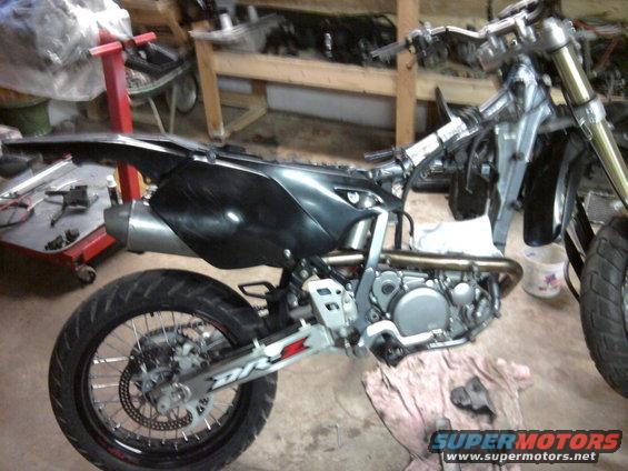 2007 Suzuki DR-Z400S motorcycle side view, black body panels, silver frame, in a workshop