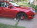 2010 Ford Fusion - A red 2010 Ford Fusion is parked on a driveway with its front wheel removed and the car supported by jack stands.
