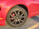 2010 Ford Fusion - Close-up of a red car's wheel and fender, showing aftermarket rims and brake calipers.