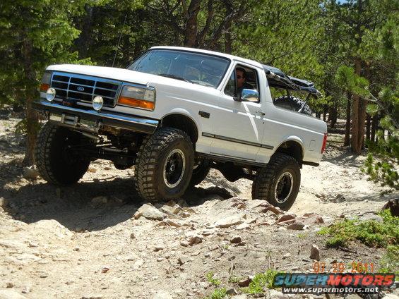 White 1996 Ford Bronco with lifted suspension and large tires driving on a rocky trail