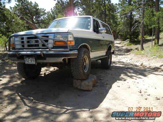 1996 Ford Bronco with brush guard on a dirt trail, front tire on a rock