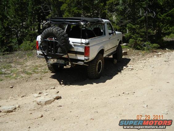 White Ford Bronco with a roof rack and rear-mounted spare tire on a dirt road