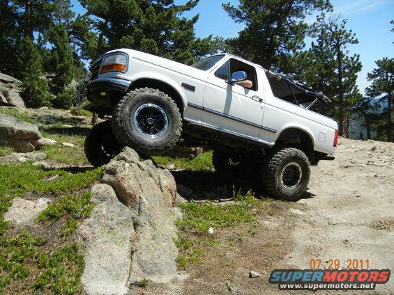 White 1996 Ford Bronco climbing over rocks on a dirt trail