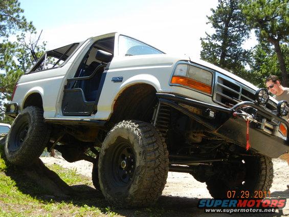 White 1996 Ford Bronco with off-road tires and bumper climbing a dirt incline