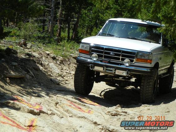 1996 Ford Bronco climbing a rocky, off-road trail with trees in the background