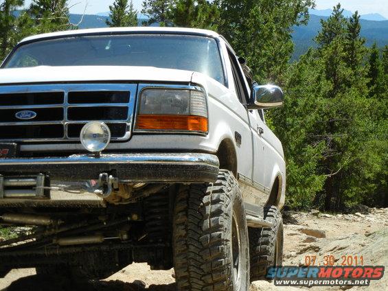 1996 Ford Bronco with large tires on a rocky, wooded trail