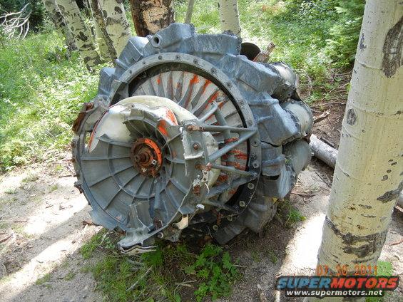 Damaged engine turbine with orange accents, resting on the ground among trees
