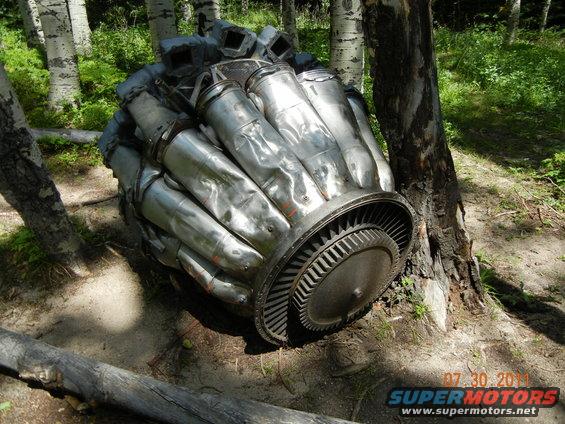 Large metal radial engine component resting on the ground near trees