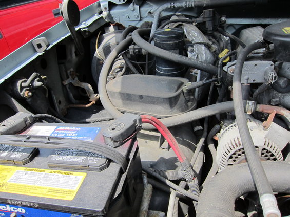 Engine bay showing ACDelco battery and various engine components. A red vehicle is partially visible on the left