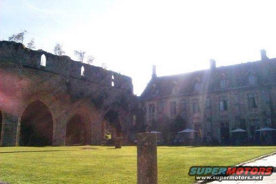 Ruined stone arches and a large building with a courtyard and umbrellas