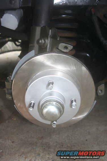 Car brake rotor with caliper and suspension components. Visible text: SUPERMOTORS.NET