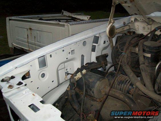 1995 Ford F-150 engine bay with white fender and black engine components. Detached white truck bed in background