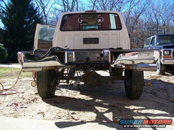 Rear view of a white Ford truck chassis with its bed removed. Another Ford truck is parked to the right