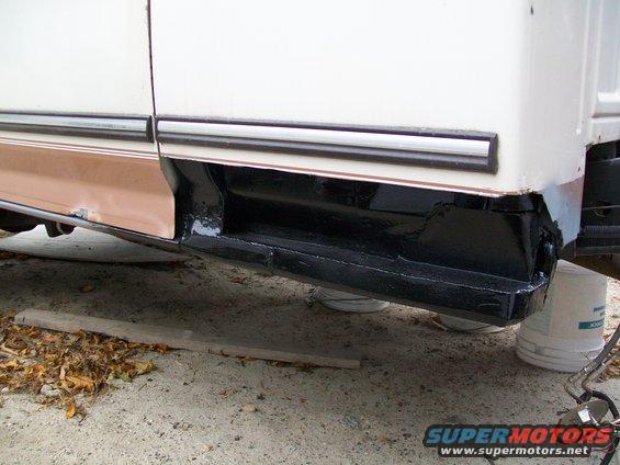 White and tan truck rocker panel with black undercoating, showing rust repair and new paint
