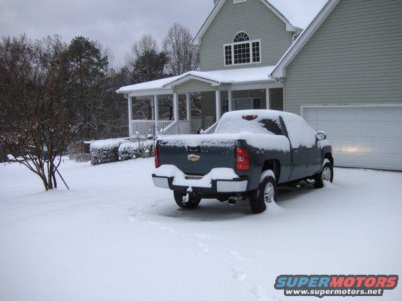 Dark blue pickup truck covered in snow parked in front of a house with a garage