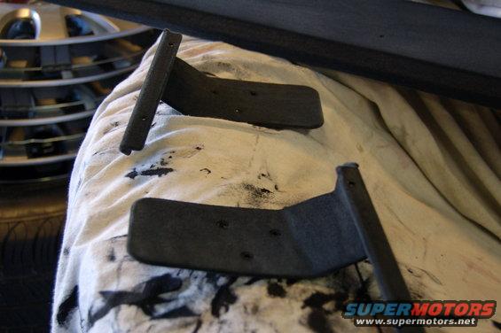 Two black metal shelf brackets with screw holes on a white cloth