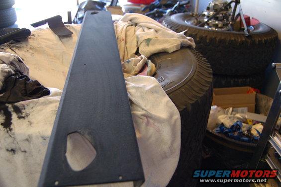 Dark gray interior shelf part with cutout, resting on cloth and tires