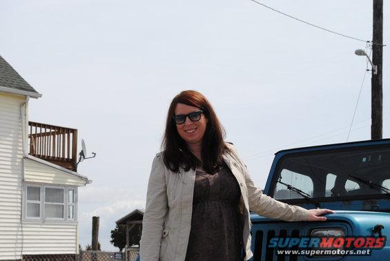 Woman in a jacket stands next to a blue Jeep Wrangler