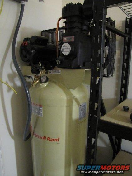 Yellow Ingersoll Rand air compressor with black motor and copper piping, next to a black metal shelf