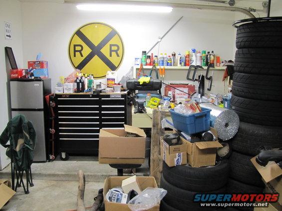 Garage scene with a tool chest, refrigerator, tires stacked, and a railroad crossing sign