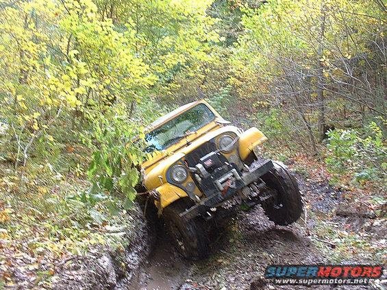 Yellow jeep driving on a muddy trail through trees