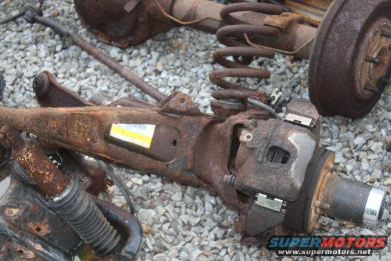 Rusty suspension assembly with brake caliper and coil spring on gravel