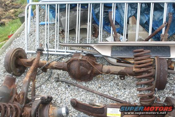 Rusty rear axle assembly with springs and brake drums, Supermotors.net logo visible