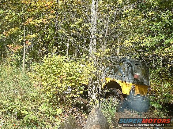 Yellow off-road vehicle with a camouflage top stuck in mud and trees