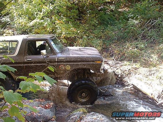 Brown 1978 Ford Bronco driving through water and rocks