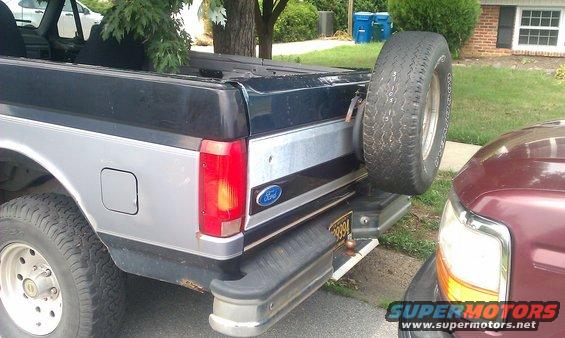 Rear view of a 1992 Ford Bronco showing spare tire on swing away carrier and a portion of another vehicle parked close by