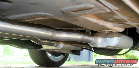 Underside of a vehicle showing a dual exhaust system with a large muffler and visible pipes