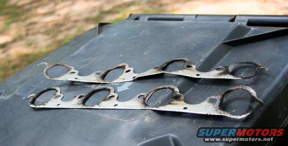 Exhaust manifold gaskets on a dark surface. SuperMotors logo visible