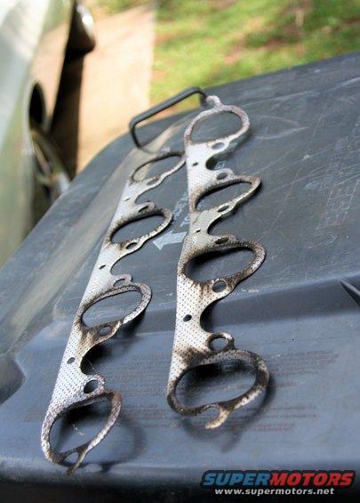 Two used exhaust manifold gaskets on a dark surface
