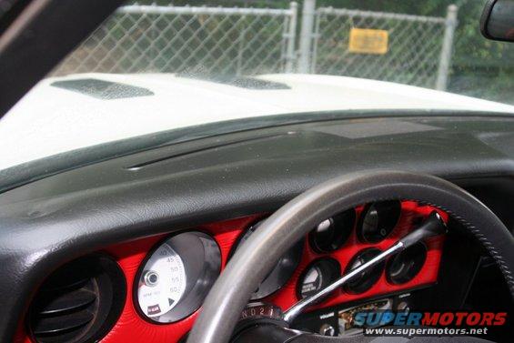 Dashboard with red trim around gauges. Steering wheel visible