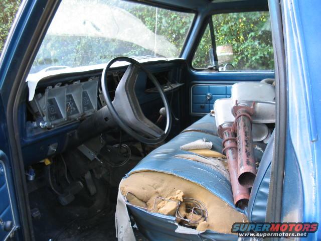 1979 Ford Bronco interior showing dashboard, steering wheel, and torn seat with exhaust pipes