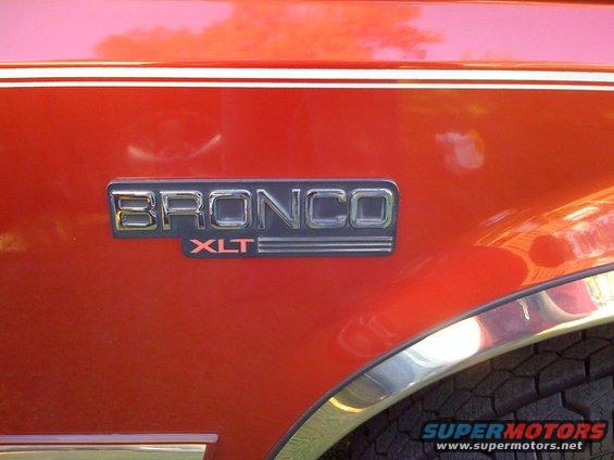 1996 Ford Bronco XLT emblem on red body panel with chrome trim and tire visible