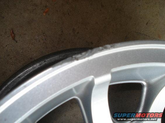 Silver alloy wheel rim with curb rash and a tire edge