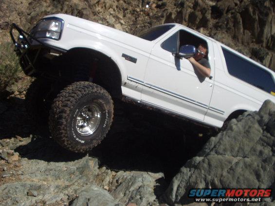 White 1993 Ford Bronco climbing over large rocks on a trail
