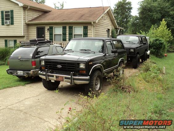 Black 1980s Ford Bronco parked in driveway next to a green SUV