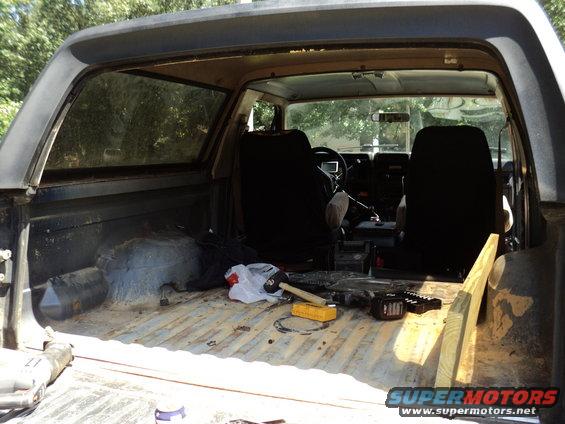 Interior of a dark blue 1980s Ford Bronco, showing front seats, dashboard, and empty cargo bed with tools