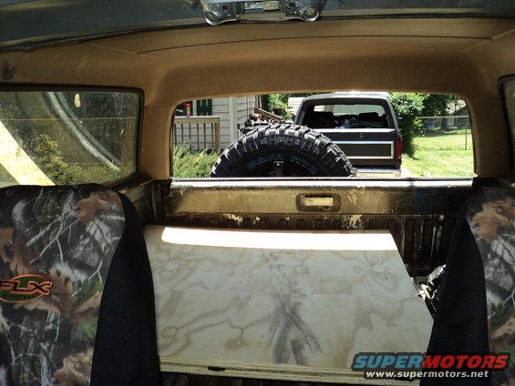 Interior view of a truck bed with spare tire; second vehicle visible through rear window