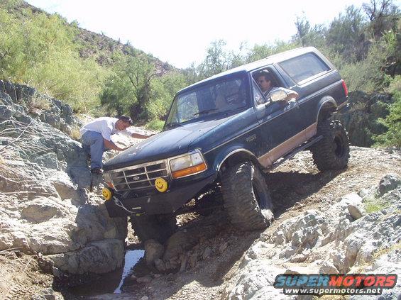 Dark green Ford Bronco with lifted suspension and large tires navigating rocky terrain