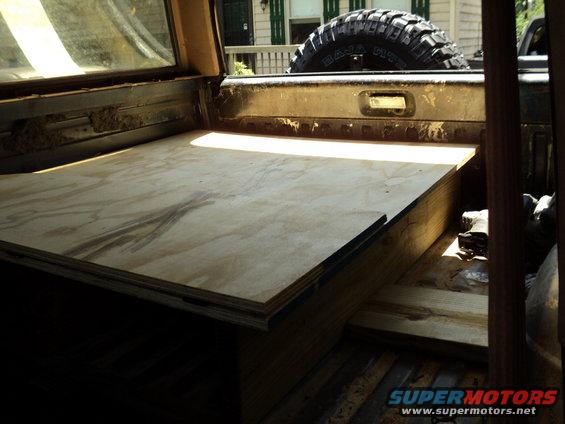 Plywood platform built inside the bed of a truck, with a spare tire visible in the background