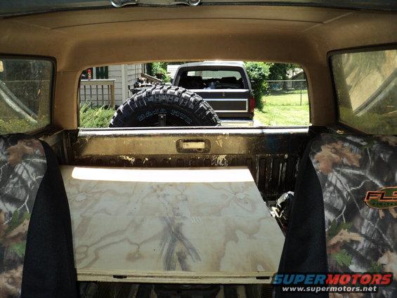 Interior view of a dark-colored Ford Bronco with a spare tire mounted on the back and a wooden platform in the bed